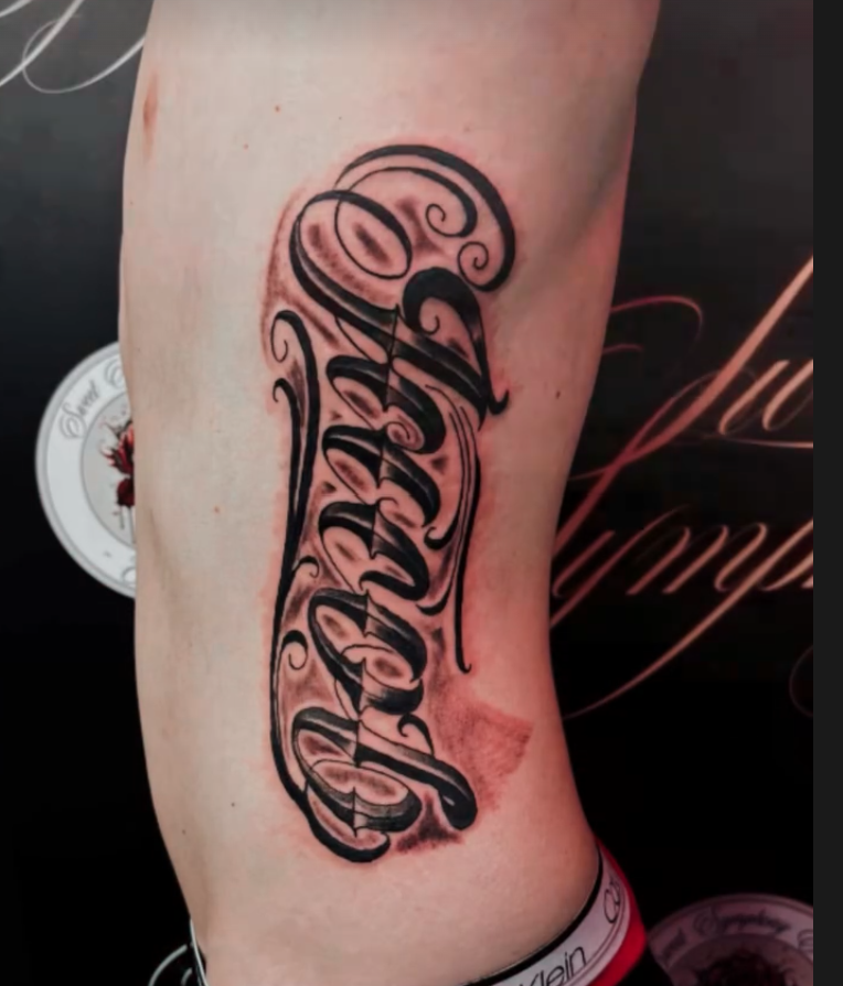 Bold cursive script name lettering tattoo on the ribs.