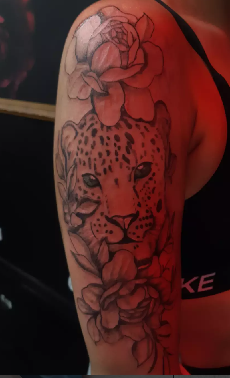 Fine-line leopard tattoo framed with roses on the upper arm.