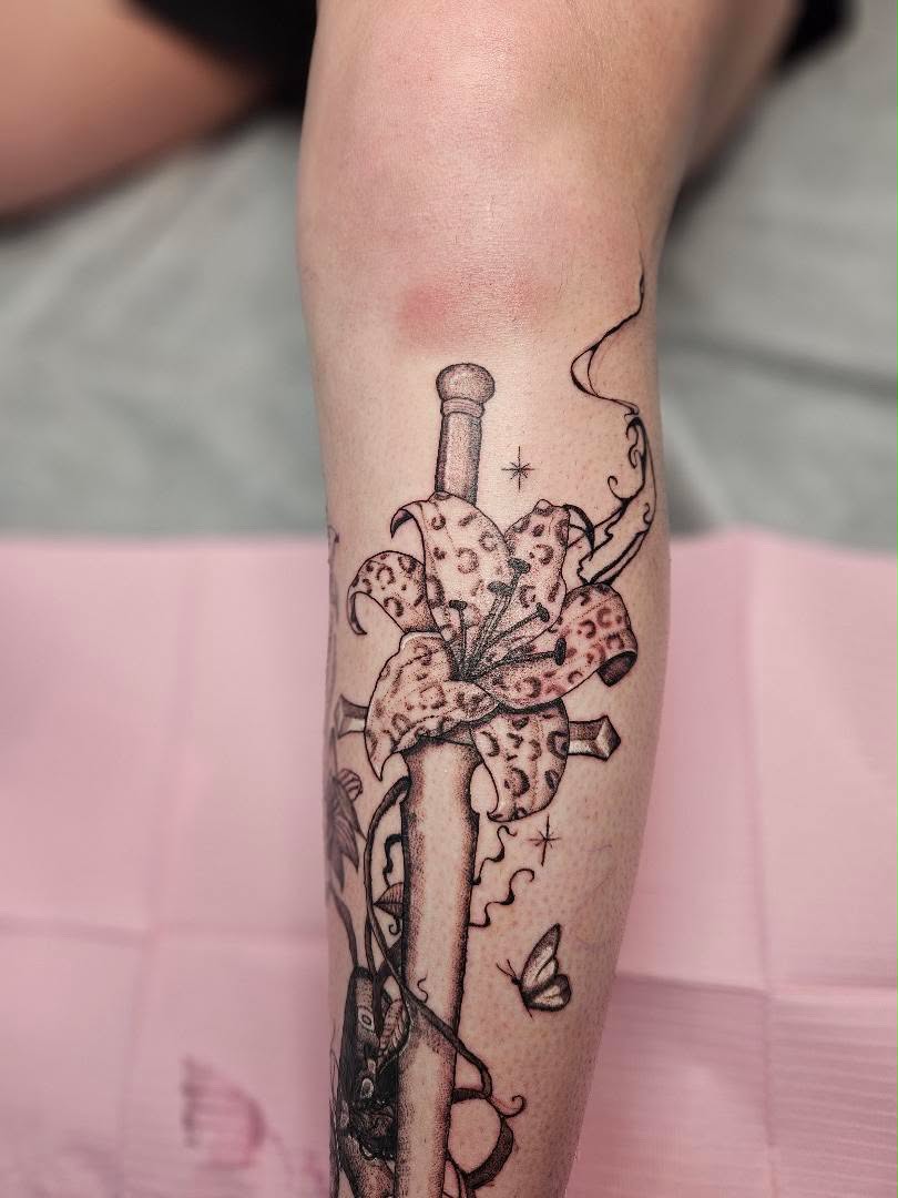 Traditional dagger tattoo with a leopard-print lily flower on the forearm.