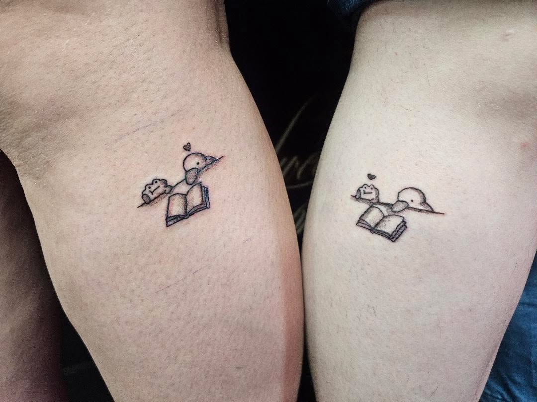 Fine-line matching duck reading a book tattoo design for a pair.