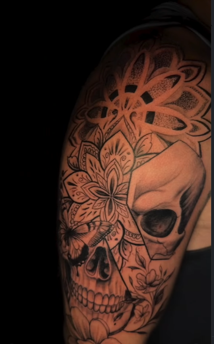 Blackwork mandala tattoo combined with a skull and butterfly on the upper arm.