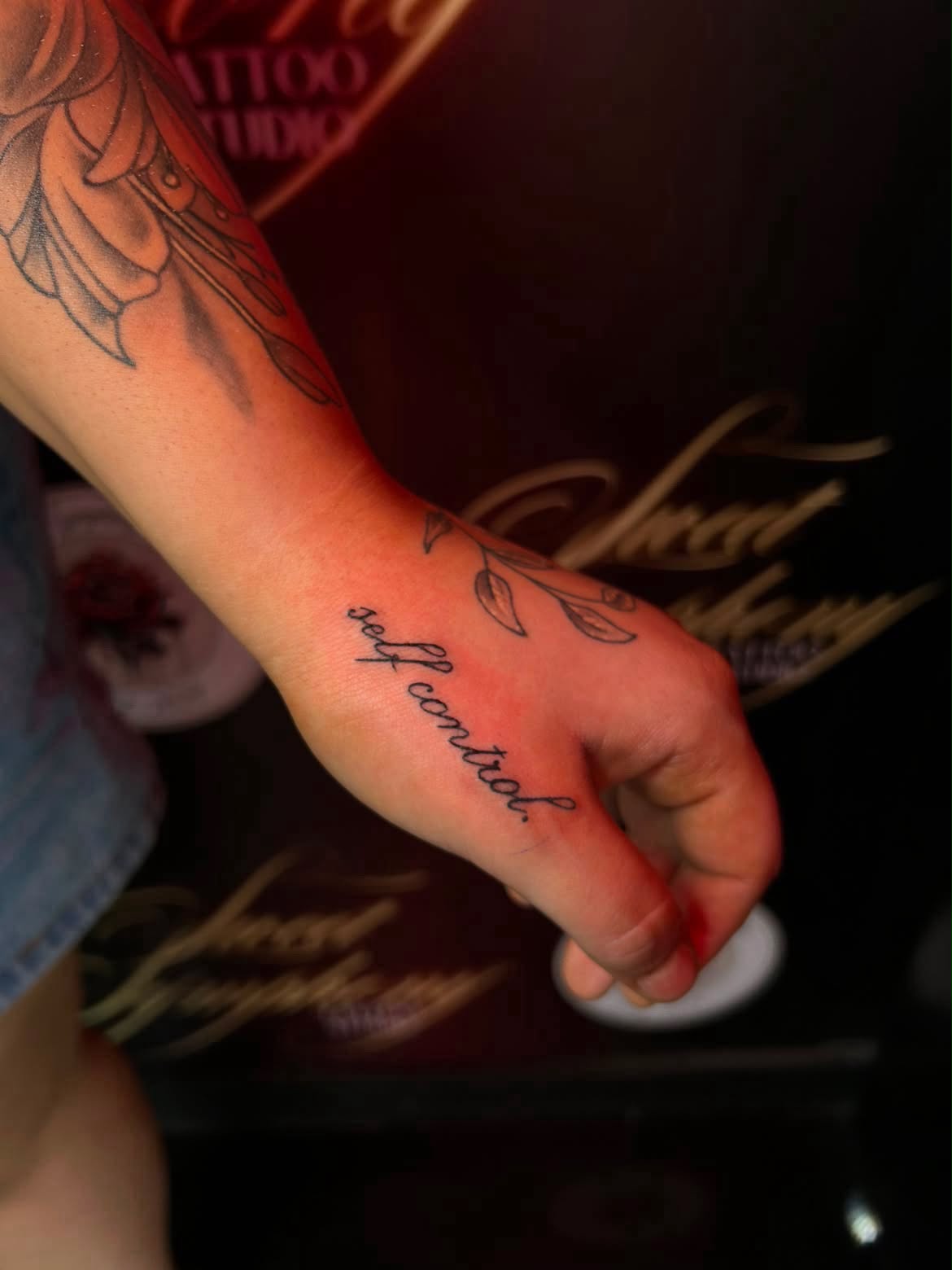 Cursive script tattoo reading 'self control' with a botanical leaf on the hand.