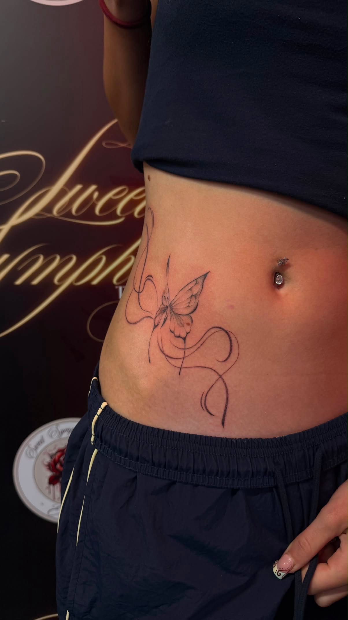 Fine-line butterfly tattoo with flowing swirl linework on the hip.
