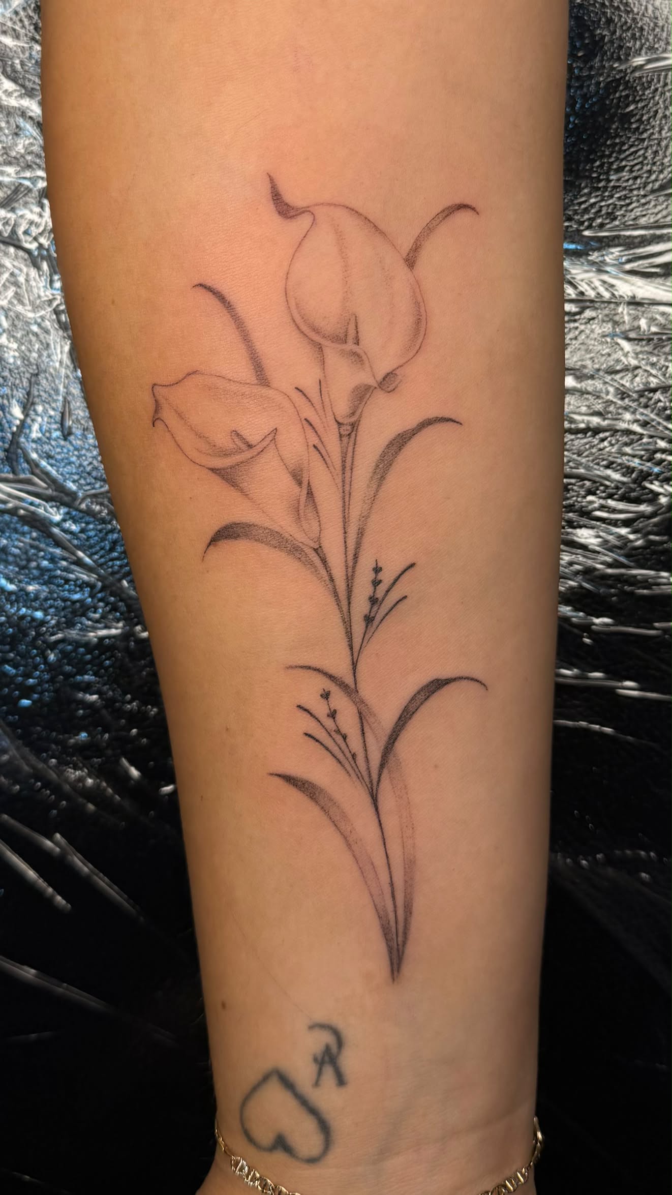 Fine-line lily tattoo with flowing ornamental swirls and dotwork shading.