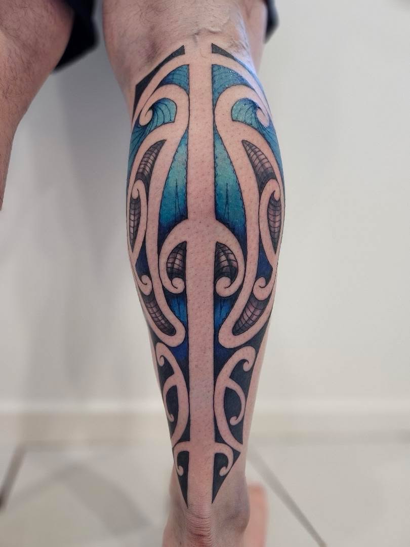 Bold tribal blackwork calf tattoo with blue-toned colour fill in a Maori-inspired pattern.