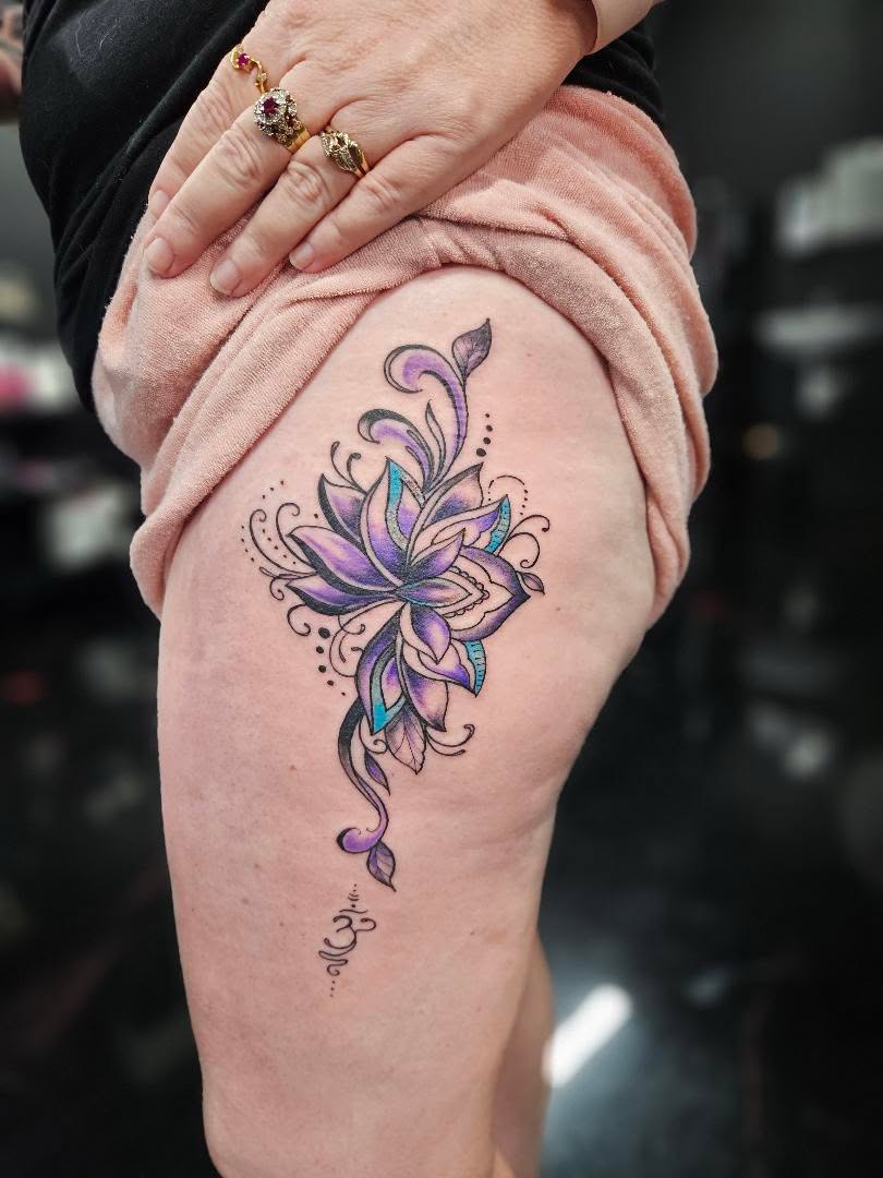 Colour fine-line lotus flower tattoo in purple and teal with dotwork accents on the hip.