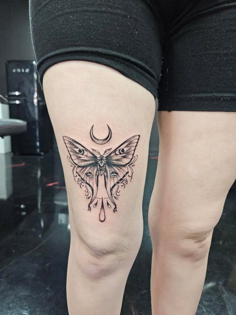Fine-line lunar moth tattoo with a crescent moon above the knee.