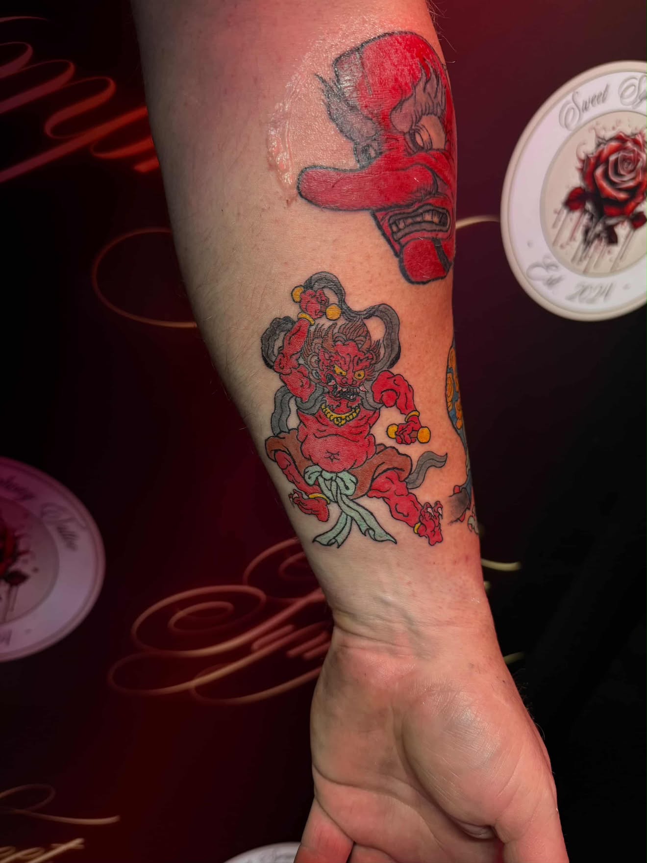 Bold colour Japanese-style oni mask and seated figure tattoo on the forearm.