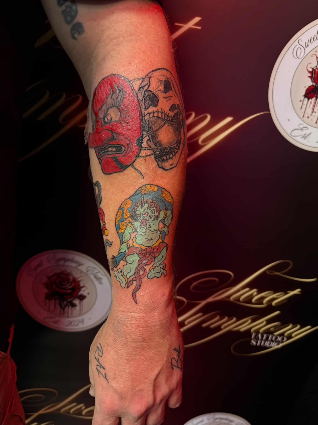 Colour Japanese-style hannya mask, skull and seated deity tattoo on the forearm.