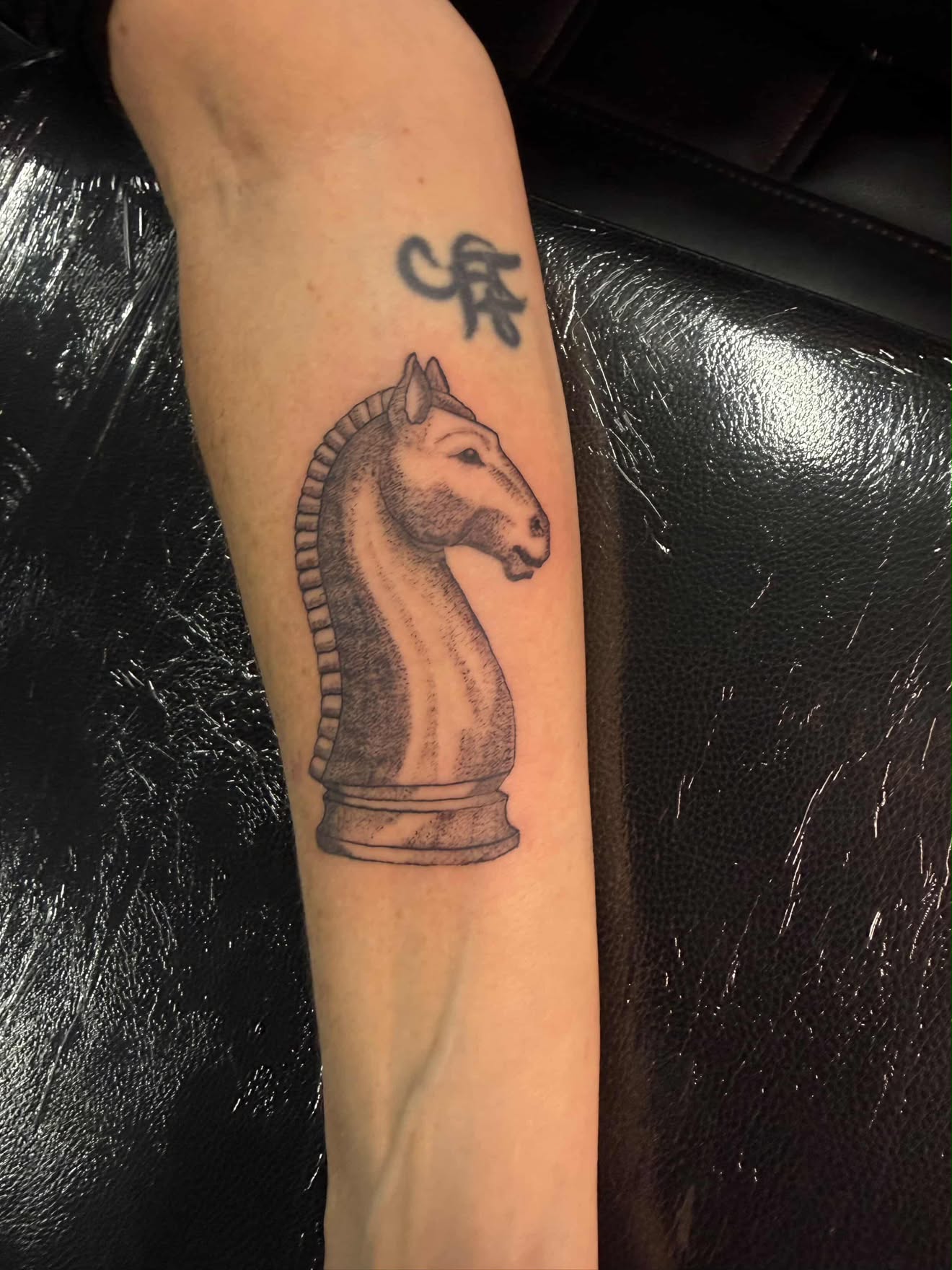 Fine-line dotwork chess knight piece tattoo on the forearm.